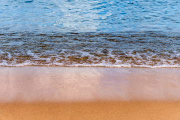 Soft waves with foam of blue ocean on the sandy beach