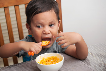 A young child about to stuff his mouth full of mac and cheese, using a spoon to independently self-feed.