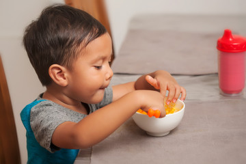 A cute toddler shows interest in eating a mac and cheese lunch, and holds spoon to self-feed.