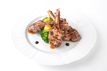 Grilled tender lamb ribs in sauce with vegetables, berries and greens. Banquet festive dishes. Fine dining restaurant menu. White background.
