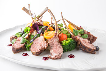 Grilled tender lamb ribs in sauce with vegetables, berries and greens. Banquet festive dishes. Fine dining restaurant menu. White background.
