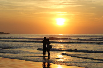 Fototapeta premium Silhouette of a couple standing close each other on the waters of a beach. Sunset with orange sky and reflections in the water.