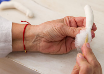 Mano de mujer mayor rellenando con algodón pieza para construir muñeca de trapo