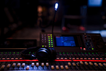 Fototapeta na wymiar Headphones lying on an advances mixing console in dim lighting in an event venue