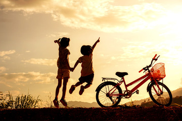 Silhouette of happy children jumping playing on mountain at sunset sky background