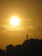 Sun setting through clouds behind silhouette of cliff diver performing daily tiki torch lighting...