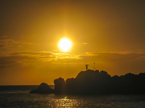 Sun setting behind silhouette  of cliff diver performing daily tiki torch lighting ceremony at black rock in Maui, Hawaii 