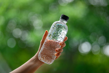 A woman's hand is holding a water bottle with a black lid, a green background and a beautiful bokeh.