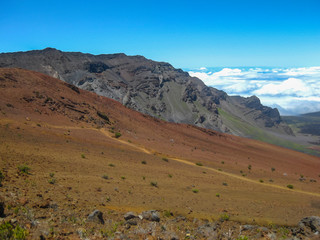Hiking trail through crater of dormant Haleakala volcano in Maui Hawaii with blue sky horizon above the clouds 
