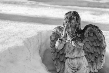 Winged angel praying and partially buried in melting snow drift