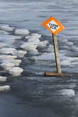 Thin ice sign and post tilting over on thawing frozen lake