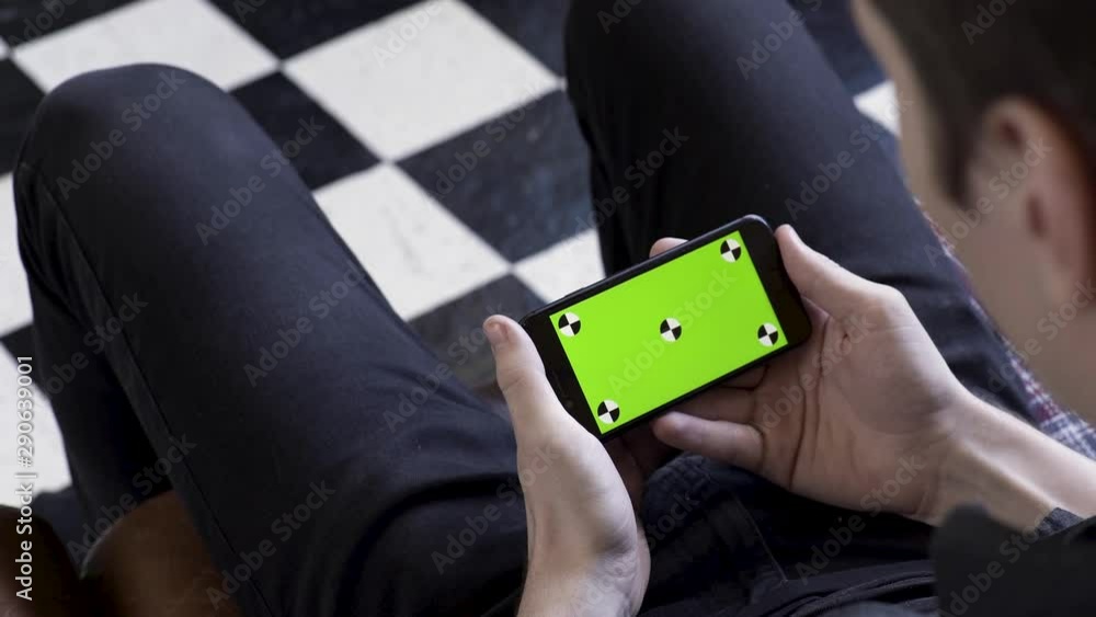 Poster business man using smart phone with green screen while sitting on a couch on checkered black and whi