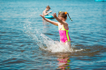 Little girl in a swimsuit bathing in the sea in summer, making a splash and running in water