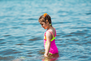 Little girl in a swimsuit bathing in the sea in summer, making a splash and running in water