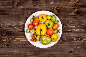 Red, yellow, green tomato in a white dish on a brown tabletop top view