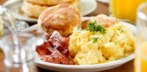 huge breakfast plate with scrambled eggs, bacon and biscuits
