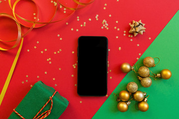 Christmas composition. Green gift box, mobile phone on red and green background with golden...