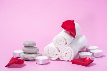 Fototapeta na wymiar White soft towels, red rose, stones and candles for skin care and spa on a pink background