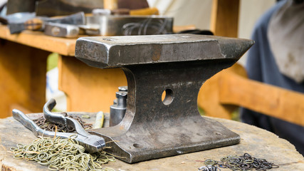anvil, tools, rings for chain mail on a log in a forge