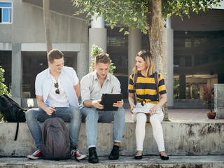 Happy university student using tablet together outside building with natural light.