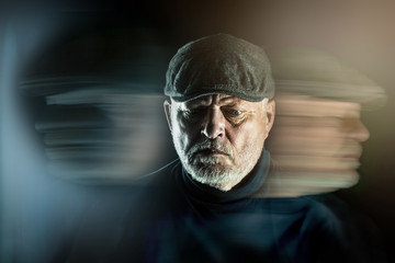 Portrait of a senior man with flat cap in front of black background. Ghostly faces surround him....