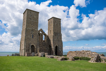 Fototapeta na wymiar An old ruin of a church now lays on the coastline, with just two towers still standing overlooking the sea, on a partially cloudy day in England, UK.