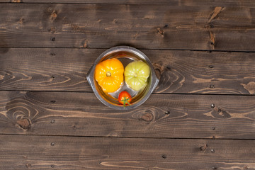 Three tomatoes in a stainless plate on a wooden table top view