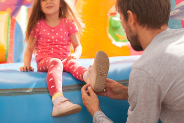 Dad puts shoes on a little girl playing on a inflatable castle