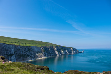 The crisp white chalk cliffs covered in a layer of bright green vegetation overlooking the sea on a clear and sunny day on the Isle of Wight.
