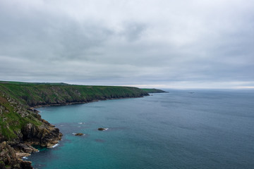 The green Cornish cliffs meets the sea on a grey and cloudy day in England, UK.