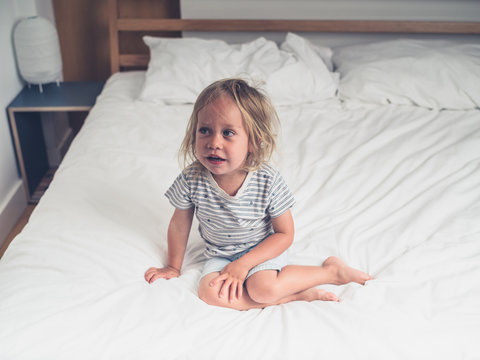 Little toddler sitting on a bed with white sheets