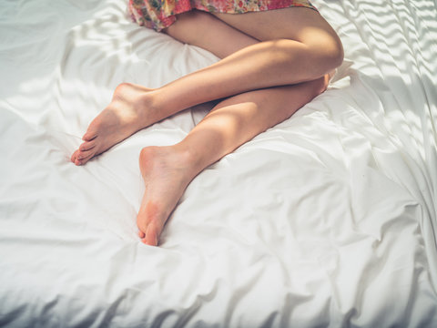 The legs of a young woman in bed on sunny day