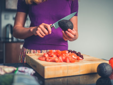 Young woman preparing salad with tomatoes and avocado