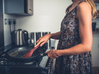 Woman cooking at gas stove with frying pan