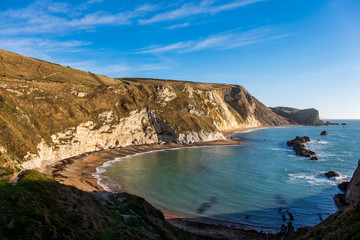 Two curved beaches are nestled against the hills overlooking the sea with a few rock formations near this cove on a clear and sunny day in England, UK.