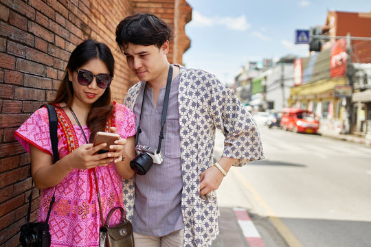 thai couple sightseeing around historical chiang mai near old city wall looking at photos on camera