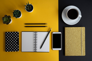 Designer desk in office with cup of coffee, smartphone, blank notebook with mock up and succulents. Yellow and black colors of desktop in modern style.
