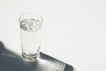 glass of water and shadow on a white background. toned. abstract. copy space