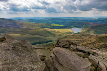Fototapeta na wymiar Rock formations in the Peak District overlooking a water reservoir as dramatic cloudy loom over the English landscape.