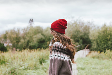 Beautiful carefree long hair asian girl in the red hat and knitted nordic sweater from behind in autumn nature park © Galina Zhigalova