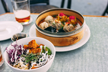 Pan-Asian food - vegetable salad bowl and different dim sums in cafe. Lunch for two with beer