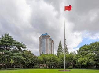A Chinese flag flying at the top of the flagpole with the background of Guanghua Twin Tower and trees at Handan Campus, Fudan University, Shanghai, China