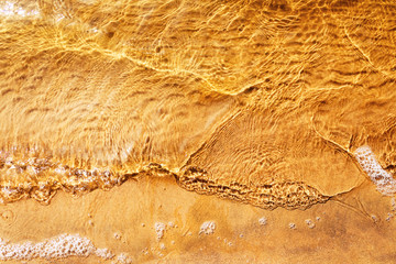 Top view of soft wave near sandy beach. Sand texture under the sea water on the beach. Nature background concept. Soft wave in the evening sun.