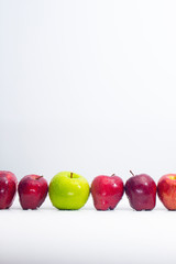 A green apple between red apples with water drops lots of white space on vertical view
