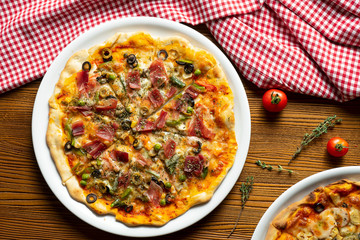 Fresh homemade pizza with prosciutto, capers, olives on a wooden background in composition with a red cloth and olive oil. Italian Cuisine. Top view food photo