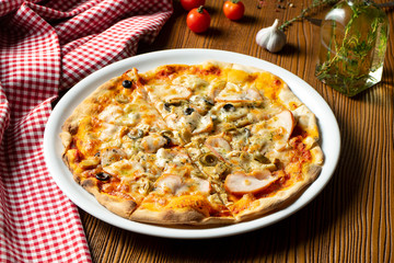 Fresh homemade pizza with ham, mushrooms and olive on a wooden background in composition with a red cloth and olive oil. Italian Cuisine. Selective focus on center of pizza