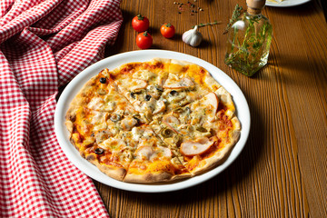 Fresh homemade pizza with ham, mushrooms and olive on a wooden background in composition with a red cloth and olive oil. Italian Cuisine. Selective focus on center of pizza