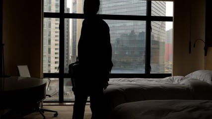 Man pick up suitcase from bed and go away from room, black silhouette against window. Slow motion shot. Guest leaving hotel, take packed bag and proceed to check out