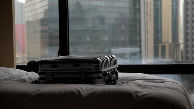 Trolley case fly and fall down on bed, dim hotel room, city buildings seen outdoors through window on background. Super slow motion shot, traveller arrive to destination after long flight