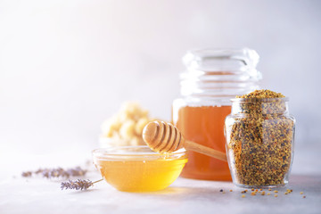 Honey products background. Honeycomb frame, bee pollen granules, honey in glass pot on grey concrete background. Copy space. Autumn harvest concept.